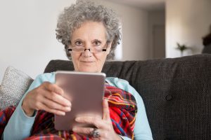 content senior lady with curly hair using modern device at home